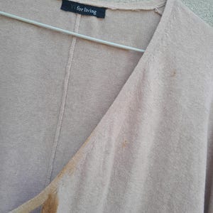 K&ouml;nnte beinhalten: Hellbraune Strickjacke mit V-Ausschnitt, an einem Metallb&uuml;gel h&auml;ngend. Das Etikett zeigt "Y's for living". Deutliche Flecken sind auf der Vorderseite vorhanden. Der Stoff wirkt weich und leicht.