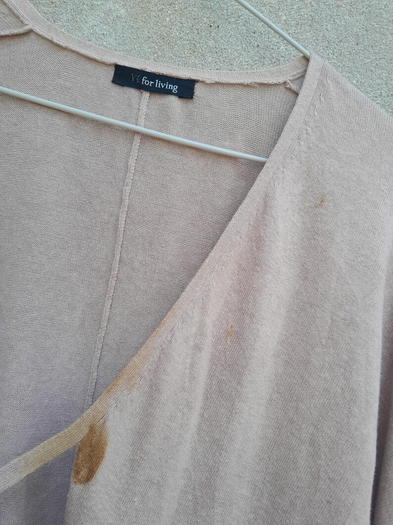 K&ouml;nnte beinhalten: Hellbraune Strickjacke mit V-Ausschnitt, an einem Metallb&uuml;gel h&auml;ngend. Das Etikett zeigt "Y's for living". Deutliche Flecken sind auf der Vorderseite vorhanden. Der Stoff wirkt weich und leicht.