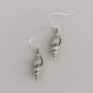 May include: A pair of silver dangle earrings featuring a detailed seashell design.