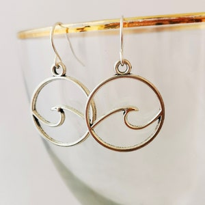 May include: Silver earrings with a wave design. The earrings are circular and have a simple, minimalist style.