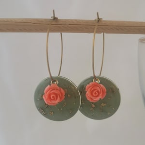 May include: A pair of green hoop earrings with a coral rose charm. The earrings have gold flecks throughout the green resin.