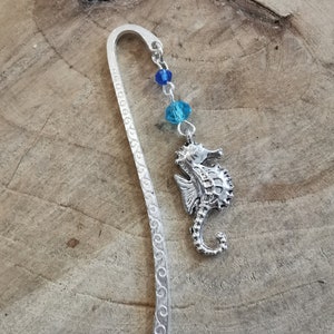 May include: Silver bookmark with a detailed scroll design and a silver seahorse charm with blue crystal beads.