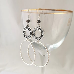 Könnte beinhalten: Silberne Ohrringe mit schwarzem Perlenanhänger und filigranem Design. Die Ohrringe haben eine Ringform mit einer strukturierten Oberfläche.
