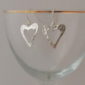 May include: A pair of silver heart-shaped earrings with a hammered texture and openwork design. The earrings hang from silver hooks.