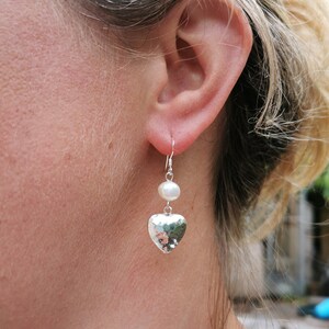 May include: Silver heart earrings with a white pearl dangle. The heart is hammered and has a textured surface.