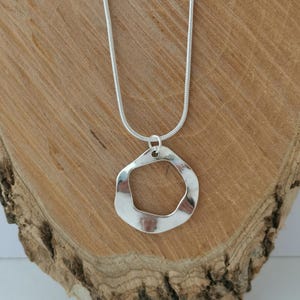 以下が含まれることがあります： 大きな不規則な形のオープンなペンダントが付いたシルバーチェーンネックレス。ペンダントはシルバー製で、滑らかで磨かれた仕上げになっています。