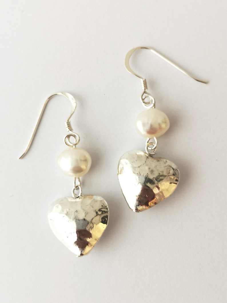 May include: Silver heart shaped earrings with a white pearl dangling from each heart.
