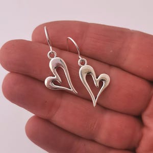 May include: A pair of silver dangle earrings featuring a heart-shaped design. The hearts are open and have a delicate, intricate design.