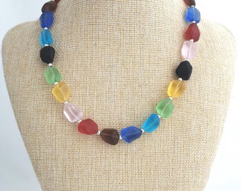 May include: A rainbow coloured glass bead necklace with silver spacers. The necklace is on a brown fabric mannequin.