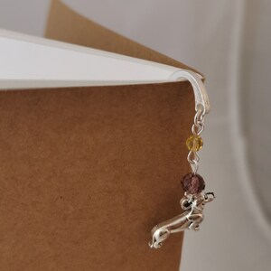 May include: Silver dachshund bookmark with a chain and purple and yellow beads.
