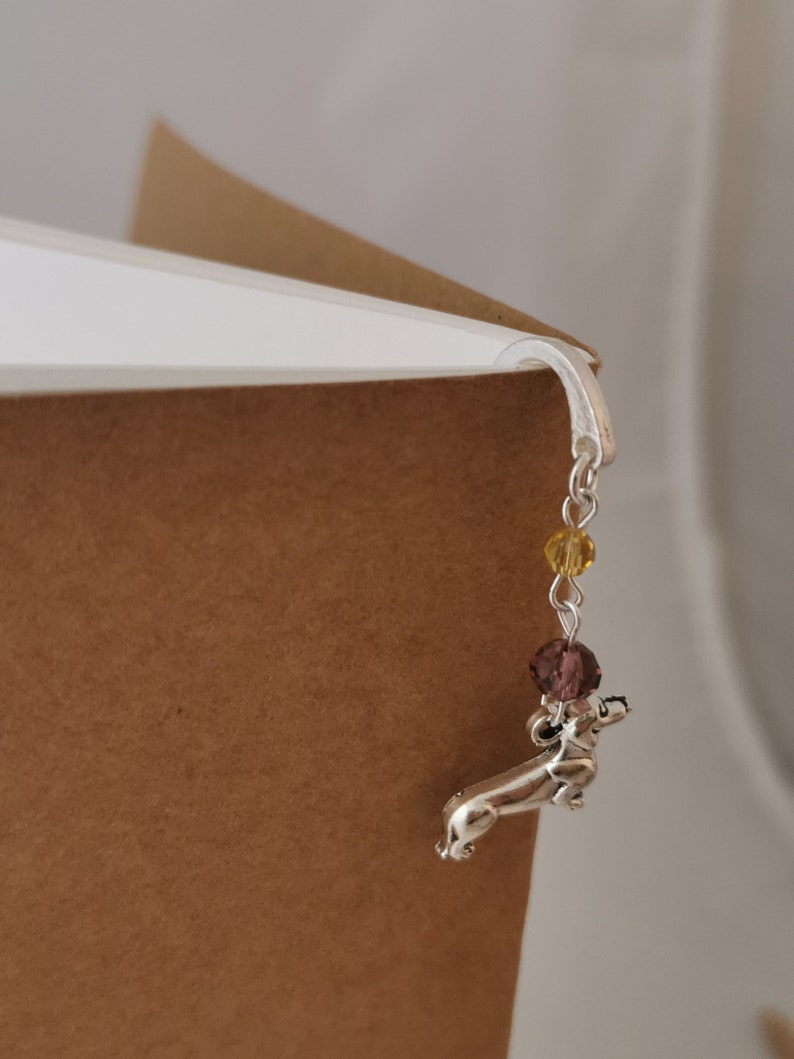 May include: Silver dachshund bookmark with a chain and purple and yellow beads.