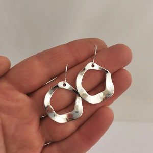 May include: A pair of silver earrings with a unique, organic shape. The earrings are made of hammered metal and have a slightly textured finish.