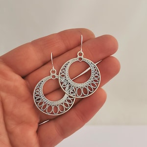 May include: Silver filigree hoop earrings with a delicate, intricate design. The earrings are lightweight and dangle from a simple hook.