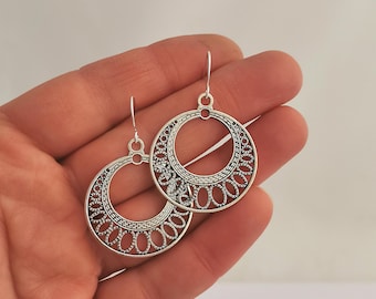 May include: Silver filigree hoop earrings with a delicate, intricate design. The earrings are lightweight and dangle from a simple hook.
