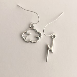 May include: A pair of silver earrings, one shaped like a cloud and the other shaped like a lightning bolt.