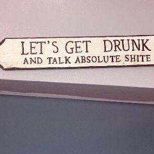Könnte beinhalten: Ein weißes Holzschild mit dem Text "Let's get drunk and talk absolute shite".