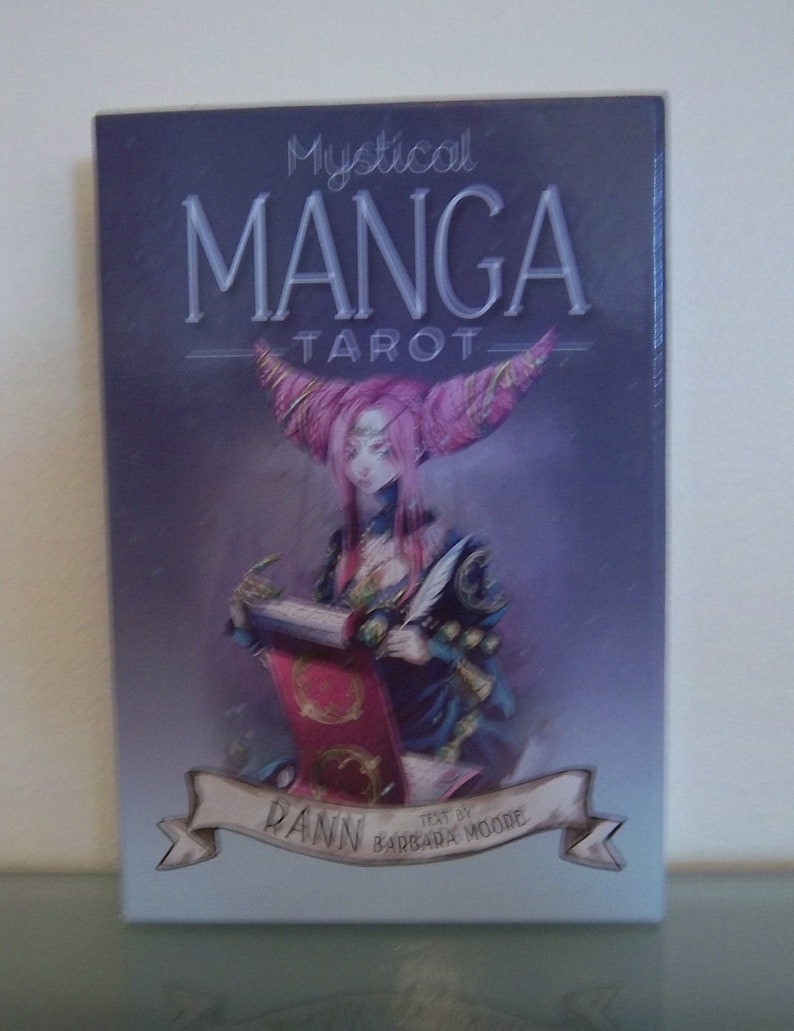 May include: Mystical Manga Tarot deck box featuring a purple and pink anime-style illustration of a woman holding a scroll. The text on the box reads "Mystical Manga Tarot" and "Dann Barbara Moore Text by".
