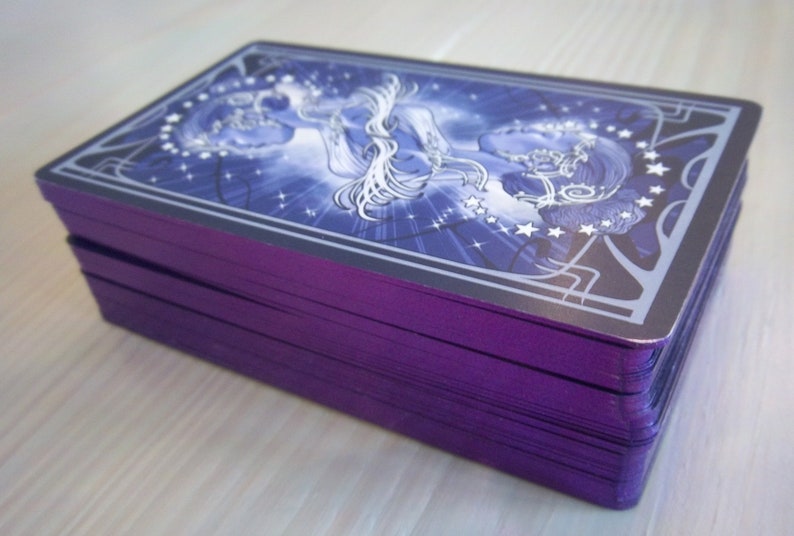 May include: A deck of tarot cards with a purple back and a blue and white illustration of a woman with stars on the front.