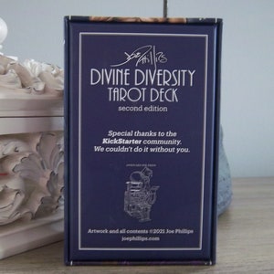 May include: A blue box with the text "Divine Diversity Tarot Deck" in white lettering. The box also includes the text "second edition" and "Special thanks to the Kickstarter community. We couldn't do it without you."