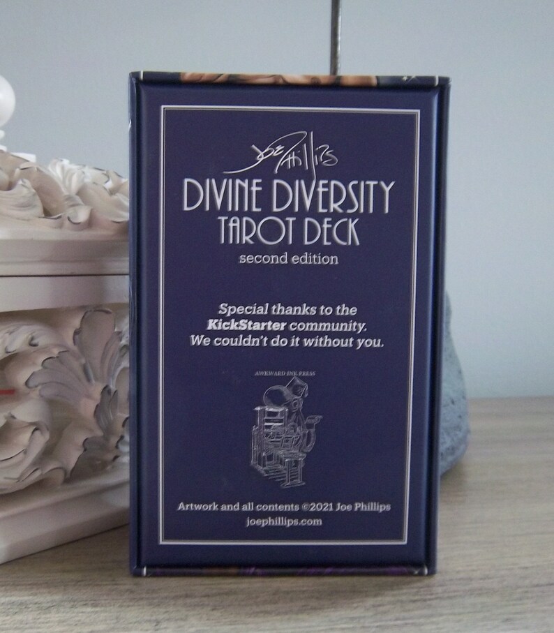 May include: A blue box with the text "Divine Diversity Tarot Deck" in white lettering. The box also includes the text "second edition" and "Special thanks to the Kickstarter community. We couldn't do it without you."