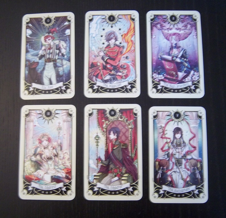 May include: A set of ten tarot cards featuring illustrations of people in various poses. The cards are numbered from 0 to 9 and have gold trim. The cards are on a light brown surface.