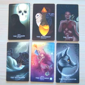 May include: Tarot card deck featuring illustrations of the Shadow, the Alchemist, the Siren, the Destroyer, the Destined, and the Shapeshifter. Each card has a unique design and imagery.