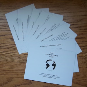 May include: A white guide with a black globe illustration and the text "Tarot Quick Reference Guide" on the front. The guide is created by Stephanie Leon Neal and produced by the Global Tarot Association. The back of the guide has a list of key words for the Major and Minor Arcana.