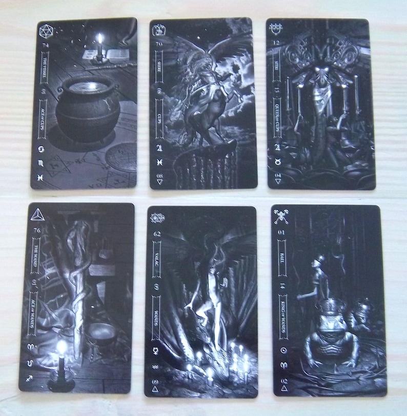 May include: Six tarot cards with black and white illustrations. The cards feature images of a cauldron, a winged creature, and other mystical figures. Each card has text and symbols.