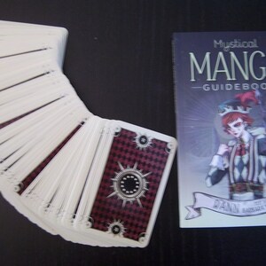 May include: A deck of Mystical Manga Guidebook tarot cards with a red and black checkered design on the back of the cards. The guidebook features a jester character with a red and white checkered costume.