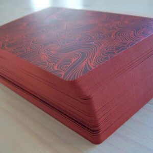 May include: A stack of red playing cards with a black and red patterned design on the top card.