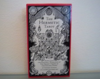 May include: A red box with a black and white illustration of a tarot deck. The box features the text "The Hermetic Tarot" and "Based Upon The Esoteric Workings Of The Secret Order Of The Golden Dawn By Godfrey Dowson US Games Systems, Inc."
