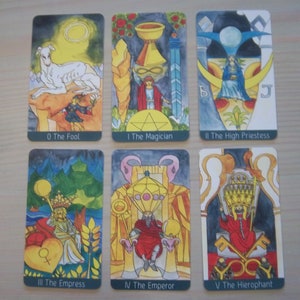 May include: Tarot card deck featuring illustrations of the Major Arcana cards, including The Fool, The Magician, The High Priestess, The Empress, The Emperor, and The Hierophant. The cards are colorful and feature detailed artwork.
