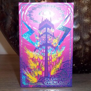 May include: A rectangular card with a fantasy illustration. The image features a tall, dark tower engulfed in flames and lightning bolts against a pink and purple background. The text "ELDRITCH OVERLOAD" is at the bottom.