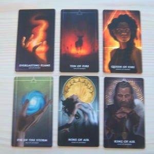 May include: Tarot cards featuring illustrations of fire, air, and water elements. The cards depict a hand holding a flame, a deer in a forest, a woman with long dark hair, a hand holding a blue orb, a woman in a white dress, and a man with a beard holding a sword.