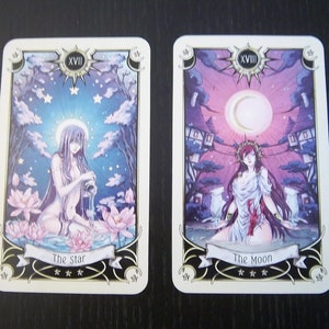 May include: Two tarot cards, The Star and The Moon, with illustrations of women in a celestial setting. The Star card features a woman pouring water from a pitcher into a pool of water with lotus flowers. The Moon card features a woman standing in a body of water with a crescent moon in the sky. Both cards have a gold border and the Roman numeral XVII.