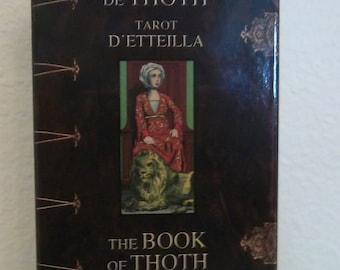 May include: A brown box with gold accents features the text "Le Livre de Thoth Tarot d'Etteilla" and "The Book of Thoth Etteilla Tarot". The box has a picture of a woman in a red dress sitting on a lion.
