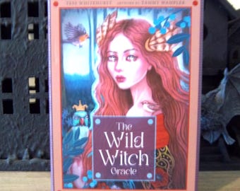 May include: A rectangular box for "The Wild Witch Oracle" deck. The box features a portrait of a woman with long red hair and a bird. The text on the box reads "ShapeShifters, Rebels & Queens".