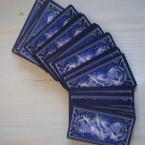May include: A deck of playing cards with a blue and silver design featuring a celestial theme. The cards are fanned out to show the backs of the cards.