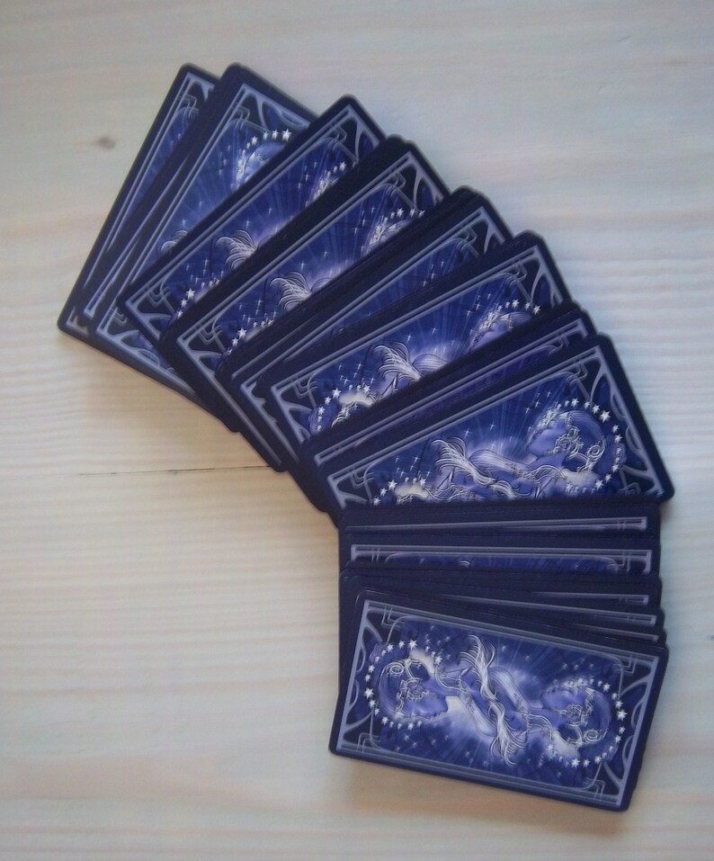 May include: A deck of playing cards with a blue and silver design featuring a celestial theme. The cards are fanned out to show the backs of the cards.