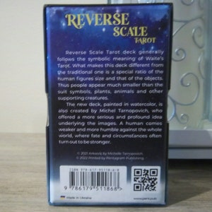 May include: A blue and gold box with the text "Reverse Scale Tarot" on the front. The back of the box has a description of the tarot deck, the ISBN number, and a QR code. The box is made in Ukraine.