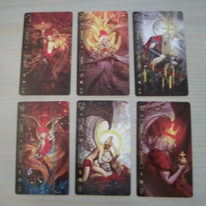 May include: Six tarot cards with gold accents and illustrations of angels. The cards are in a vertical row, with the top card showing a red and gold angel with wings spread wide. The second card shows a white angel with wings spread wide. The third card shows a black and white angel with wings spread wide. The fourth card shows a red and gold angel with wings spread wide. The fifth card shows a white angel with wings spread wide. The sixth card shows a black and white angel with wings spread wide.