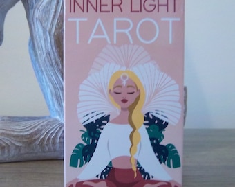 Könnte beinhalten: Eine rosa Box mit den Worten "Inner Light Tarot" in weißen Buchstaben. Die Box zeigt eine farbenfrohe Illustration einer meditierenden Frau mit einer weißen Krone vor rosa Hintergrund.