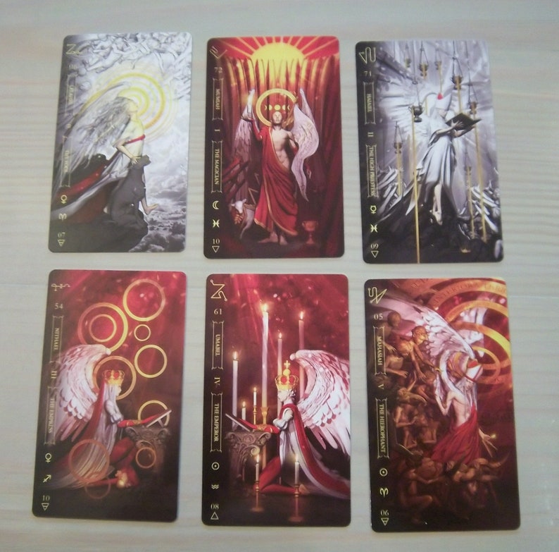 May include: Set of ten tarot cards featuring illustrations of angels with wings and gold accents. The cards are numbered 1-10 and have the names of the angels written on them. The cards are on a gray surface.