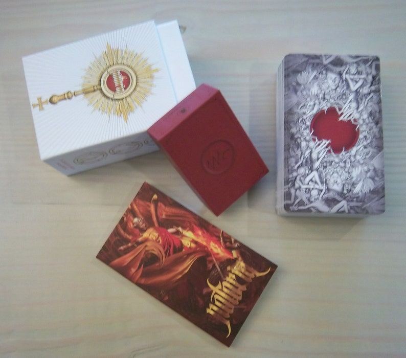May include: A red box with a white circle and the word "WITCH" inside. A white box with a gold design and a cross. A deck of cards with a black and white design and a red circle in the center. The cards have the word "Witchcraft" printed on the side.