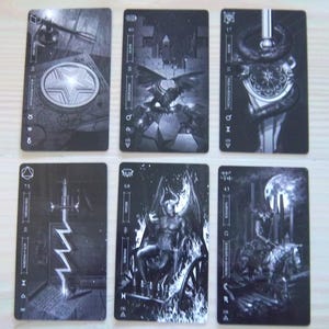 May include: Six black and white tarot cards are displayed, each featuring detailed illustrations. The cards depict various symbolic imagery, including a star, a winged creature, a serpent, a sword, a demonic figure, and a rider on horseback. The cards have text and symbols.