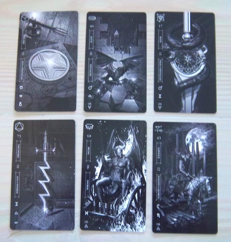 May include: Six black and white tarot cards are displayed, each featuring detailed illustrations. The cards depict various symbolic imagery, including a star, a winged creature, a serpent, a sword, a demonic figure, and a rider on horseback. The cards have text and symbols.