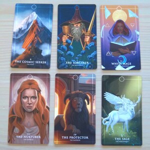 May include: Set of ten tarot cards with colourful illustrations and gold accents. The cards feature images of a cosmic seeker, a sorcerer, a white mage, a nurturer, a protector, a sage, a lover, a chariot, a strength, and a hermit.
