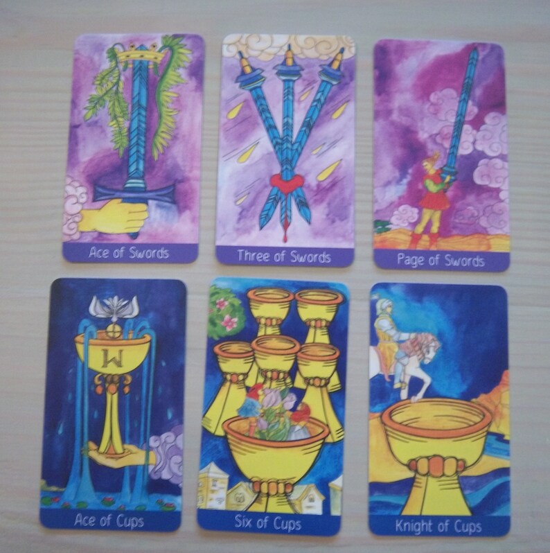 May include: Tarot card spread with six cards, including Ace of Swords, Three of Swords, Page of Swords, Ace of Cups, Six of Cups, and Knight of Cups. The cards are illustrated with watercolor paintings on a purple background.
