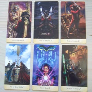 以下が含まれることがあります： 2列に並べられた6枚の長方形のタロットカード。上段：Ace of Swords、Two of Swords、Page of Swords II。下段：Ace of Oars、Six of Oars、Knight of Oars。各カードには、鮮やかな色彩で描かれた詳細なファンタジーイラストが施されています。