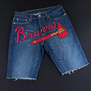 May include: Blue denim shorts with a red embroidered "Braves" logo and a tomahawk design.